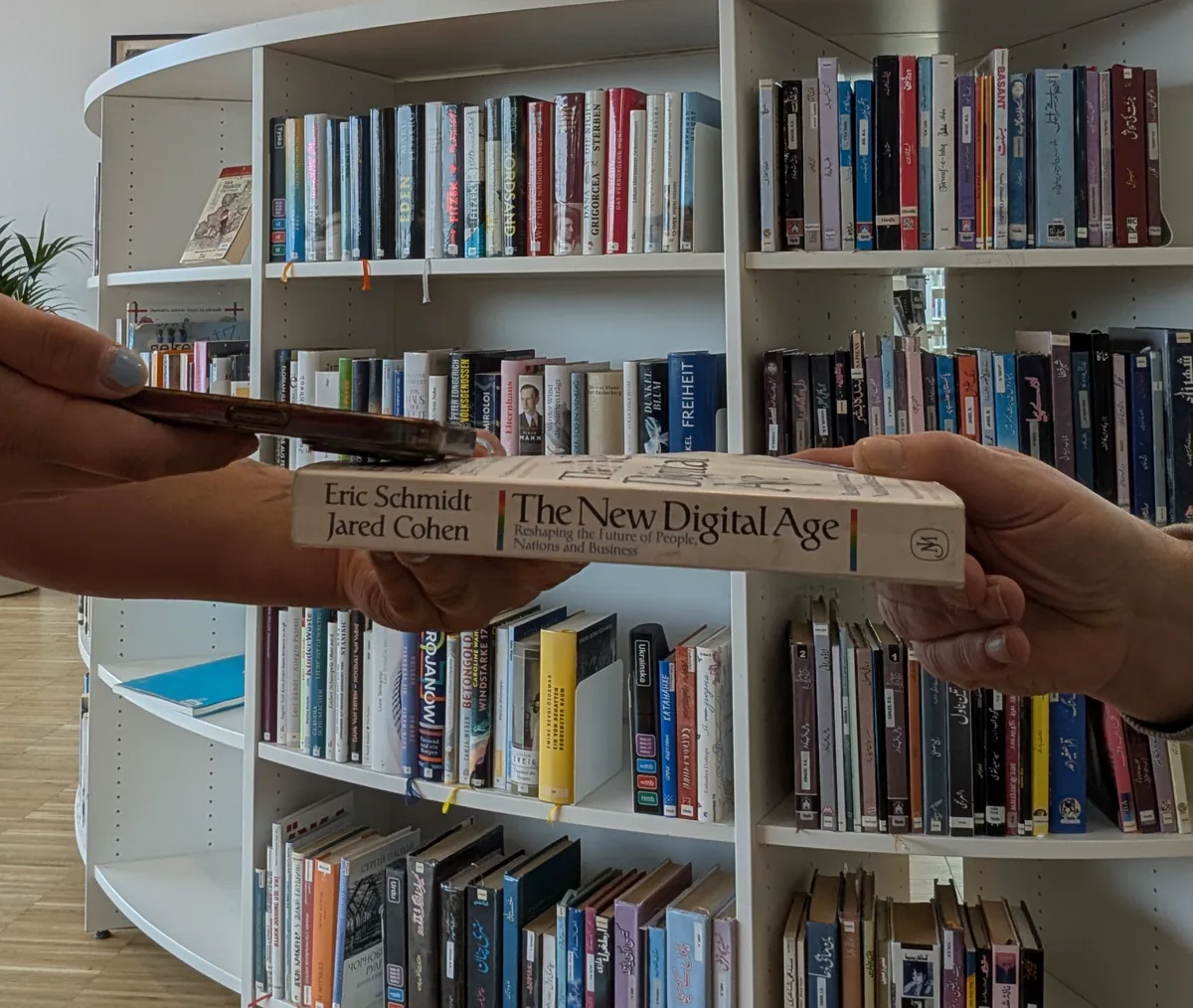 The book passed from one pair of hands to another in front of a library shelf.