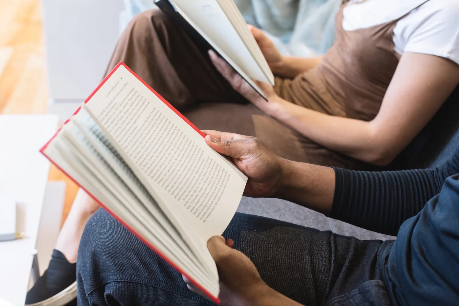 Two people sitting side by side at home, each holding an open paper book.