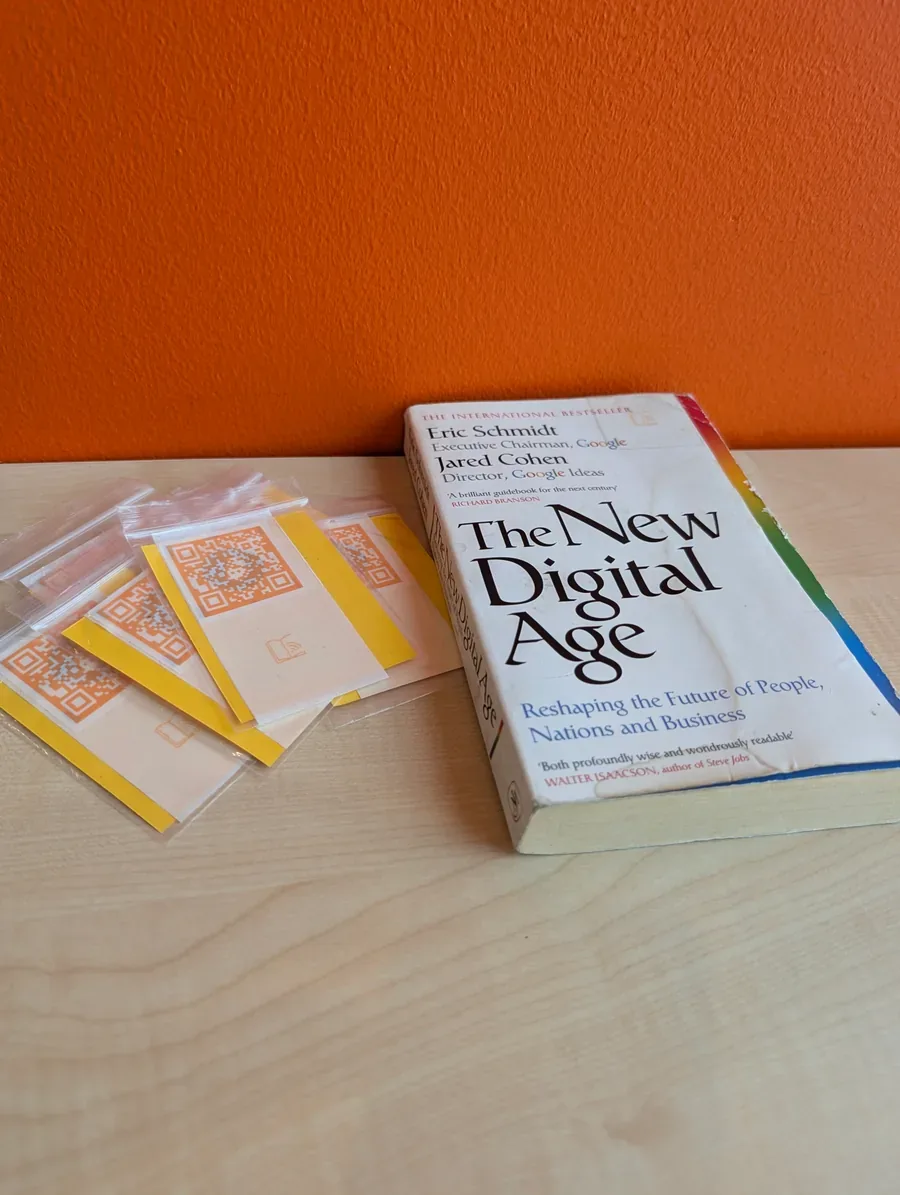 A stack of αBook label stickers in small bags beside the worn copy of The New Digital Age.